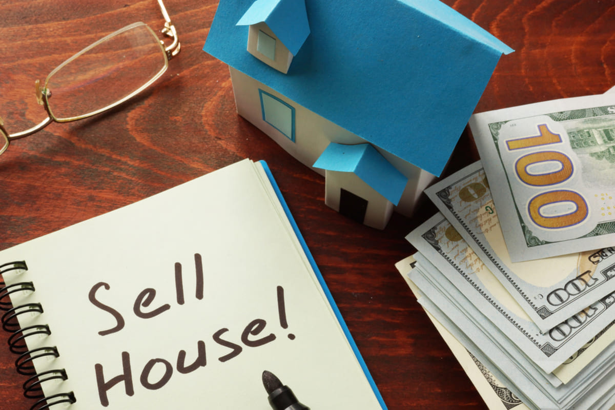 A house next to cash and a notebook that says Sell House!, buy my house for cash concept house key